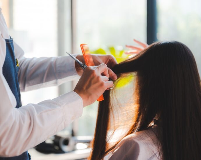 stylist cutting woman's hair in salon, Hairdresser coiffure trimming brown hair with scissors